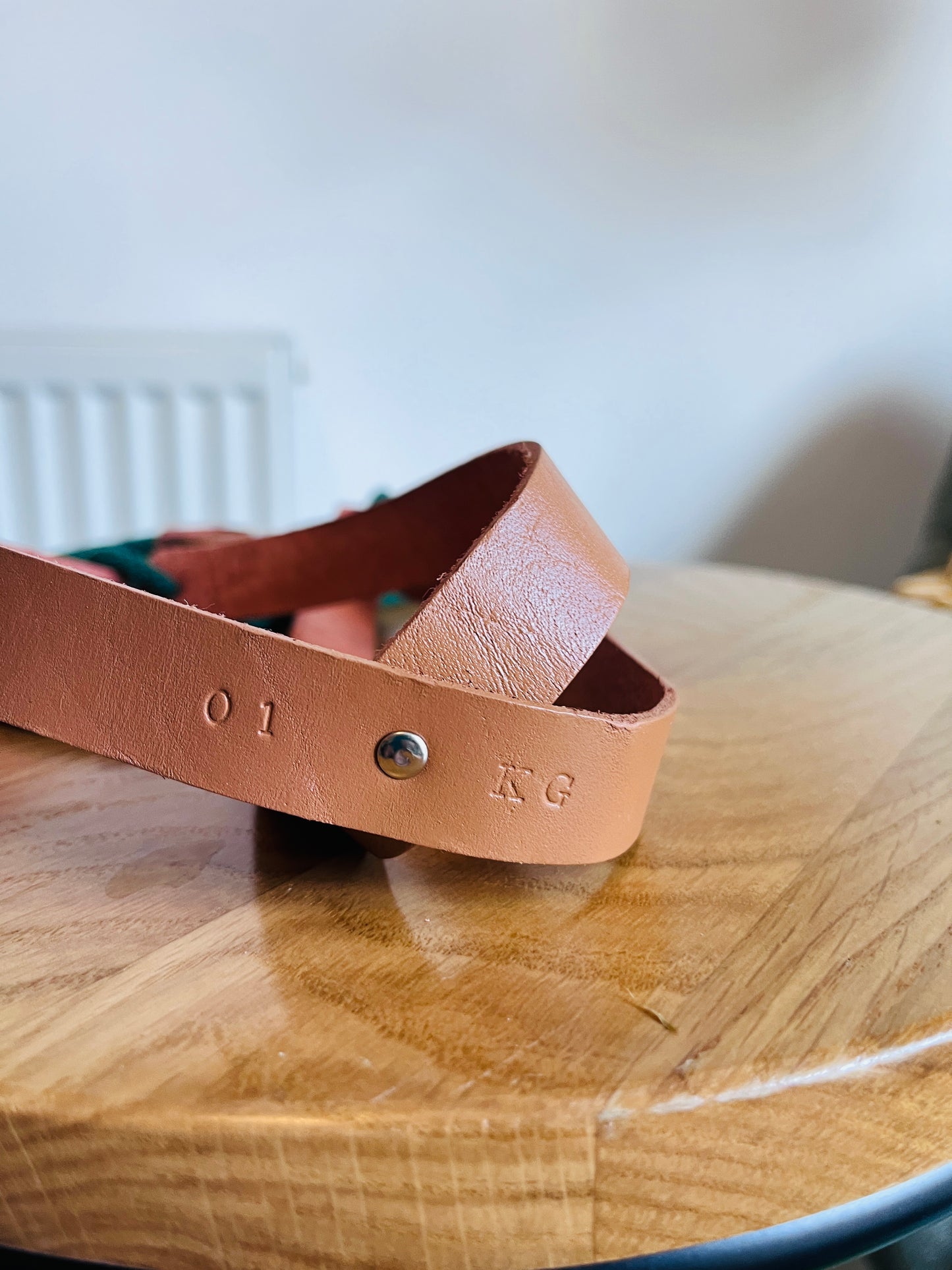 Brown leather strap with '01 KG' engraving on a wooden surface